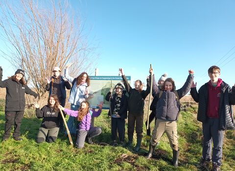 Diverse group of young people with shovels stand outside a nature reseve, smiling at the camera