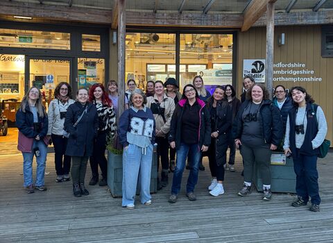 A big group of women are gathered together in front of the Nene Wetlands Visitor Centre, smiling. 