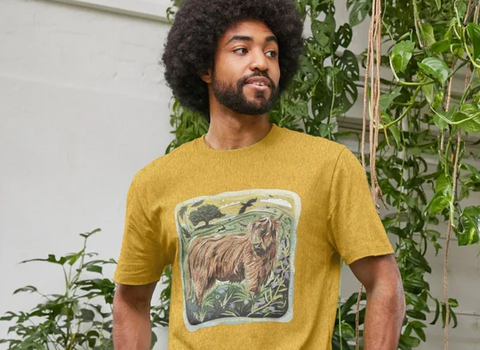 A mn stands wearing a mustard yellow t-shirt with an illustration of a highland cow