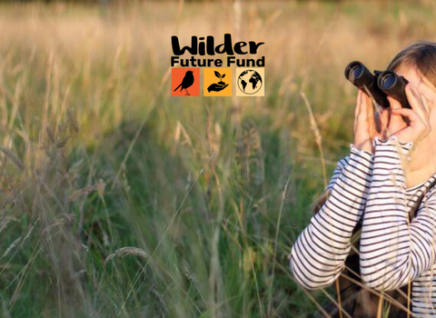A young girl looks through binoculars on a grassy meadow. The Wilder Future Fund logo is displayed in the middle.